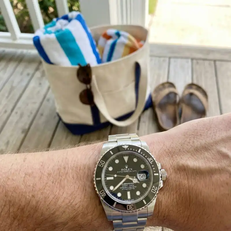 Close-up of a luxury wristwatch on a wrist, with a beach tote bag ready in the background.